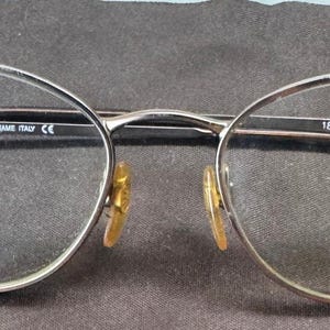May include: Silver-framed eyeglasses with oval lenses. The glasses have a Giorgio Armani frame and are marked "Frame Italy." The nose pads are gold-toned. The frame measurements are 51mm lens width, 18mm bridge width, and 135mm temple length.