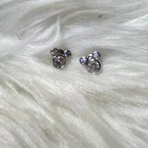 May include: A pair of silver earrings with clear crystal stones in the shape of Mickey Mouse heads.