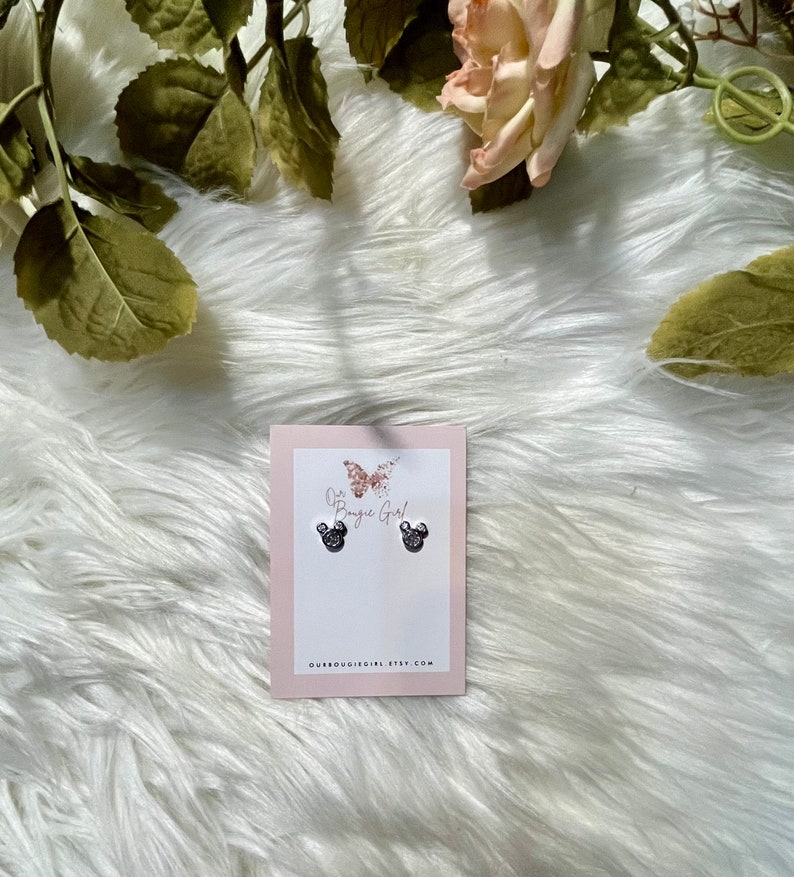 May include: A pair of silver stud earrings featuring a black and white Mickey Mouse design. The earrings are presented on a white card with the text "Our Boutique Girl" and a butterfly graphic.