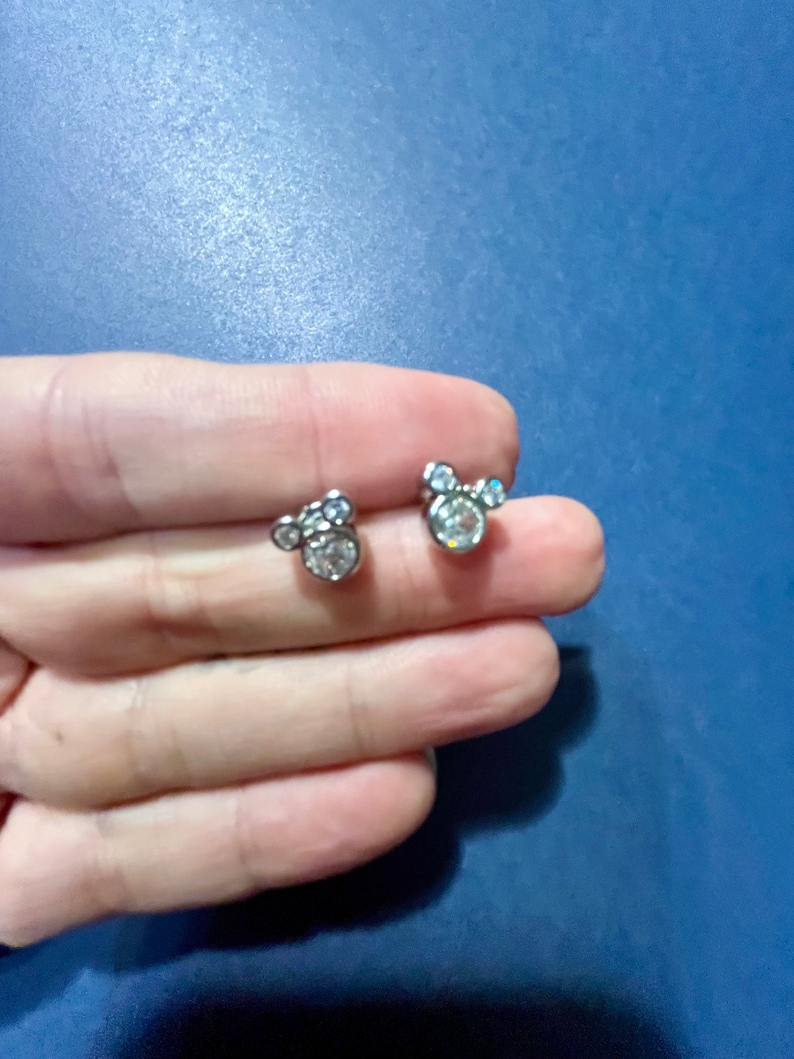 May include: A pair of silver stud earrings with a Mickey Mouse design featuring clear rhinestones.