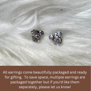 May include: A pair of silver earrings with clear crystal stones in the shape of Mickey Mouse heads.