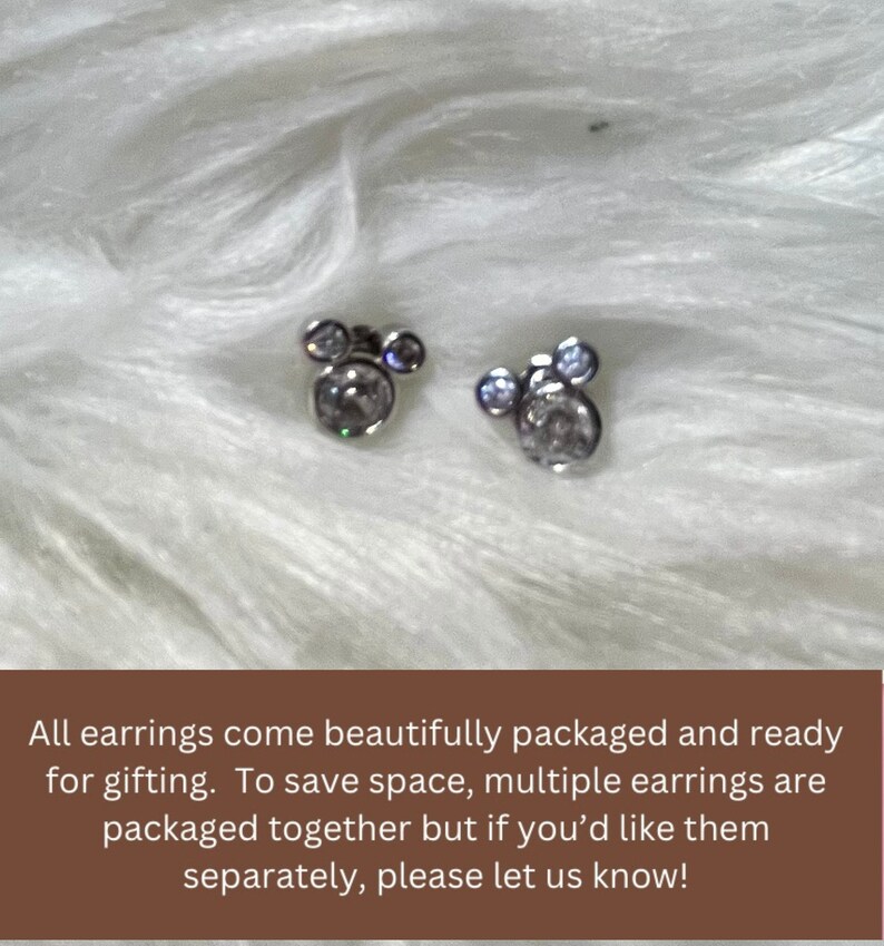 May include: A pair of silver earrings with clear crystal stones in the shape of Mickey Mouse heads.
