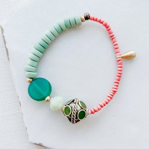 以下が含まれることがあります： 緑とピンクのビーズブレスレット。シルバーのチャームには緑色のアクセントが施されています。ブレスレットは丸いビーズで作られており、繊細で女性らしいスタイルです。