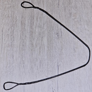 Puede incluir: Un cordón negro con dos bucles en cada extremo, sobre una superficie de madera clara.