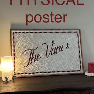May include: A framed mosaic art piece with the text "The Vani's" in a cursive font. The mosaic is white with a red border and accents. The frame is a dark wood. The words "PHYSICAL poster" are above the frame.