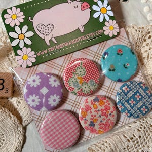 May include: A collection of six fabric-covered buttons with floral and geometric patterns. A business card with a pig illustration and the text "www.vintagepolkadotpig.etsy.com" is visible. A wooden block with the letter "B" and the number "3" is also present.