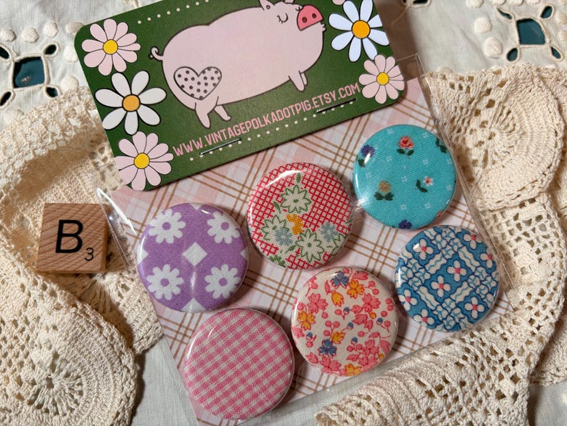 May include: A collection of six fabric-covered buttons with floral and geometric patterns. A business card with a pig illustration and the text "www.vintagepolkadotpig.etsy.com" is visible. A wooden block with the letter "B" and the number "3" is also present.