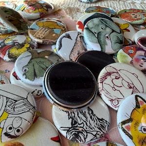 May include: A collection of round magnets with various cartoon illustrations. The magnets feature images of animals, people, and other whimsical designs in bright colors. Some magnets have a glossy finish and a black magnetic backing.