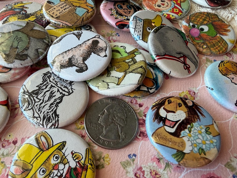 May include: A collection of vintage pinback buttons with various cartoon animal illustrations, including a bear, lion, and elephant. A US quarter is in the center. The buttons are white with colorful designs.