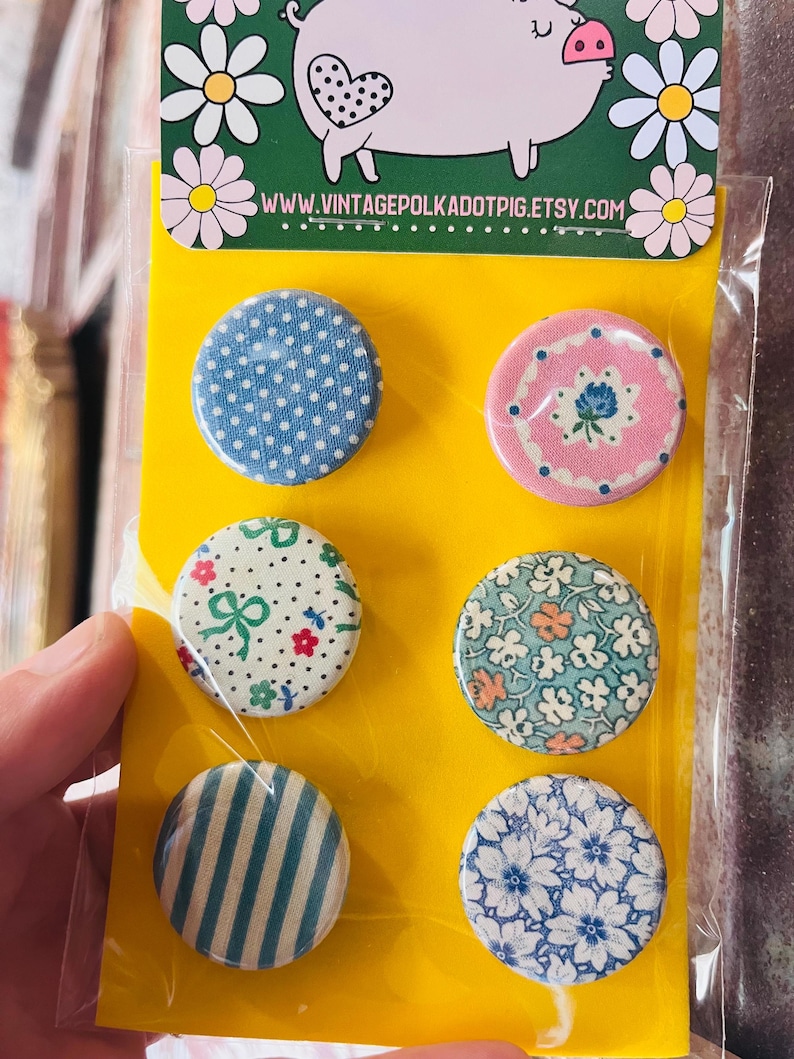 May include: Set of six round pinback buttons with various patterns, including polka dots, floral designs, and stripes. The buttons are displayed on a yellow backing card with a pig illustration and the website address www.vintagepolkadotpig.etsy.com.