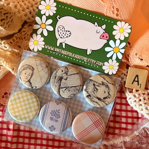May include: A set of six circular pinback buttons packaged with a green display card featuring a white pig illustration and the text WWW.VINTAGEPOLKADOTPIG.ETSY.COM. The buttons display various designs including a person, animals, and patterns.