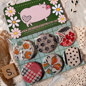 May include: A set of six round fabric-covered buttons with various floral and geometric patterns. A business card with a pig illustration and the text "VINTAGEPOLKADOTPIG.ETSY.COM" is visible. A wooden Scrabble tile with the letter "S" is also present.