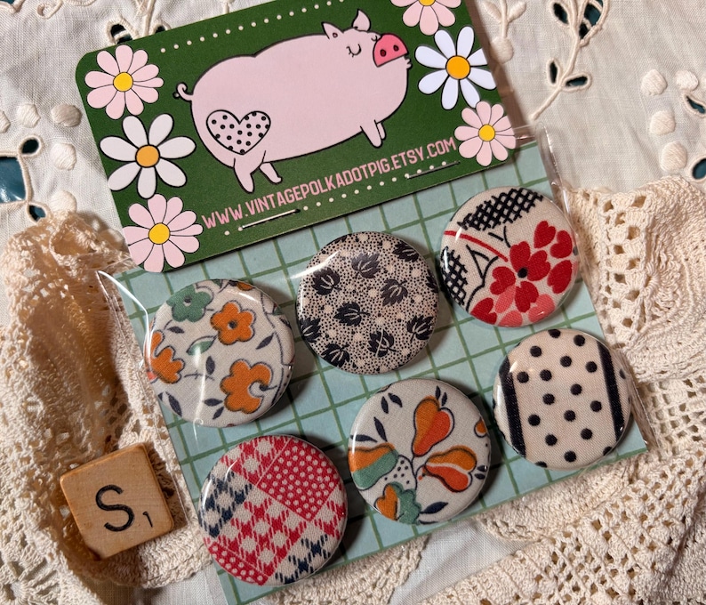 May include: A set of six round fabric-covered buttons with various floral and geometric patterns. A business card with a pig illustration and the text "VINTAGEPOLKADOTPIG.ETSY.COM" is visible. A wooden Scrabble tile with the letter "S" is also present.