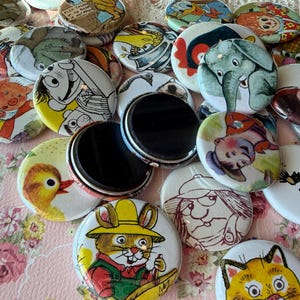 May include: A collection of colorful, round magnets with various cartoon illustrations. The magnets feature images of animals, characters, and scenes in a variety of colors. Some magnets have black magnetic backs.