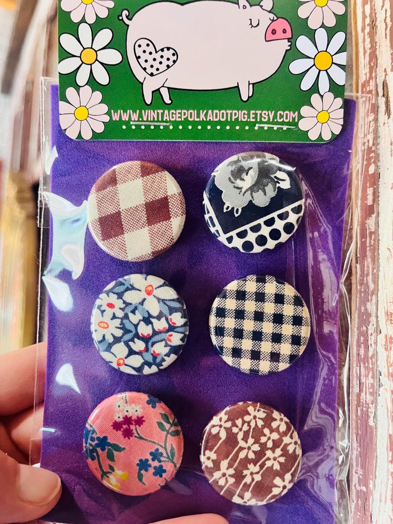 May include: A set of six round fabric-covered buttons with various patterns, including gingham, floral, and polka dots. The buttons are displayed on a purple background, with a pig illustration at the top. The website address www.vintagepolkadotpig.etsy.com is visible.