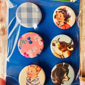 May include: A set of six round vintage-style pinback buttons. Designs include a blue and white gingham pattern, a girl in a red dress, a pink floral pattern, a cow, a boy in a striped shirt, and a bear. The top of the package has the text "WWW.VINTAGEPOLKADOTPIG.ETSY.COM".
