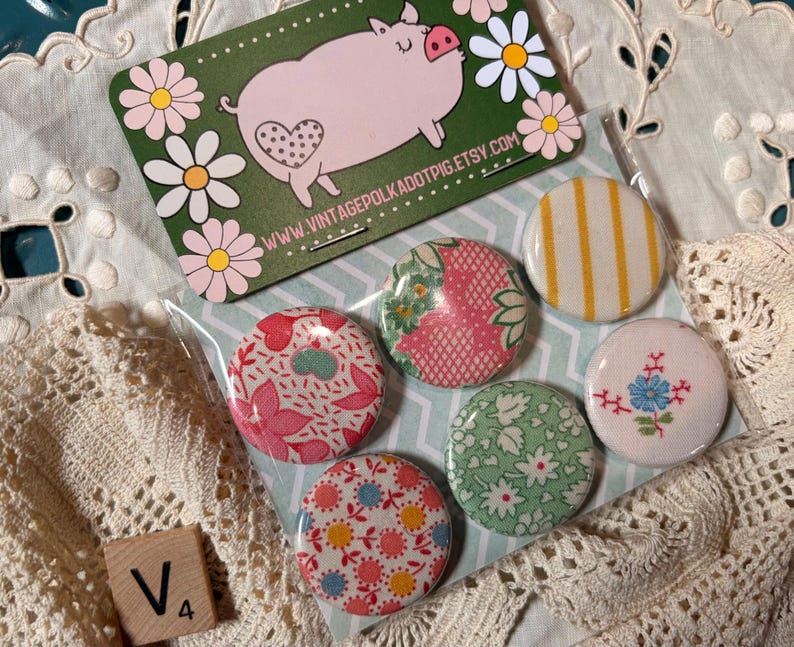 May include: A collection of six round pinback buttons with various floral and patterned designs. A green card with a pig illustration and the text "www.vintagepolkadotpig.etsy.com" is also visible. A wooden tile with the letter "V" and the number "4" is in the image.