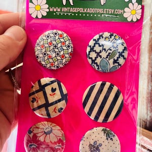 May include: A set of six round decorative magnets with various patterns, including geometric shapes, floral designs, and stripes. The magnets are displayed on a bright pink backing with a pig illustration and the website www.vintagepolkadotpig.etsy.com.