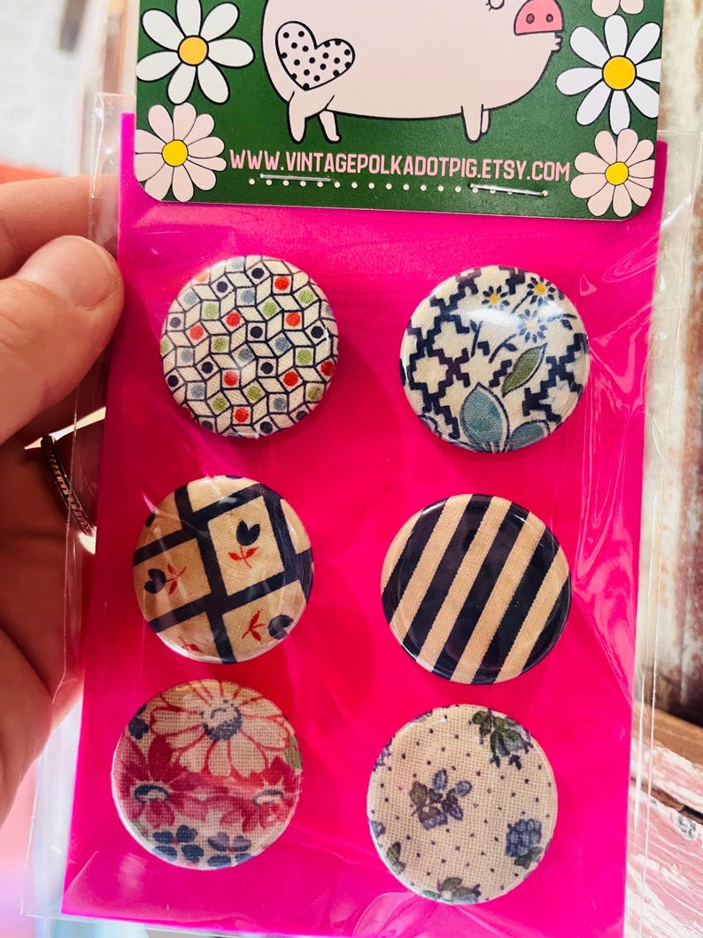 May include: A set of six round decorative magnets with various patterns, including geometric shapes, floral designs, and stripes. The magnets are displayed on a bright pink backing with a pig illustration and the website www.vintagepolkadotpig.etsy.com.