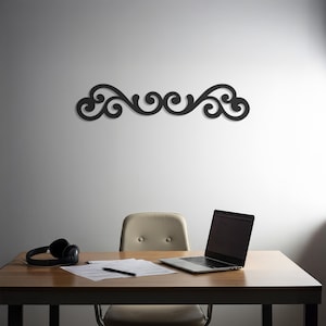 Puede incluir: Una pieza de arte mural decorativa negra con un diseño simétrico de desplazamiento. El arte está montado en una pared blanca sobre un escritorio de madera. También se ven un portátil, auriculares y una silla de oficina.