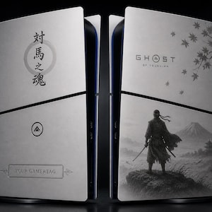 Op de afbeelding: Een lichtgrijze console skin met de tekst "Ghost of Tsushima" en Japanse karakters. Het ontwerp toont een samoerai-krijger die uitkijkt over een berglandschap. Het onderste paneel heeft ruimte voor een gamertag.