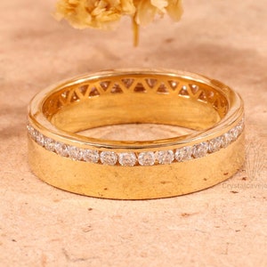 Puede incluir: Una banda de oro con una fila de pequeños diamantes y un borde decorativo con patrón.