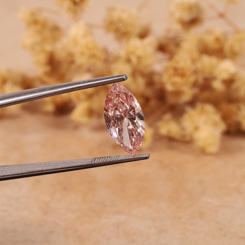 May include: A light pink marquise-shaped gemstone held by tweezers. The gemstone is faceted and has a brilliant shine.