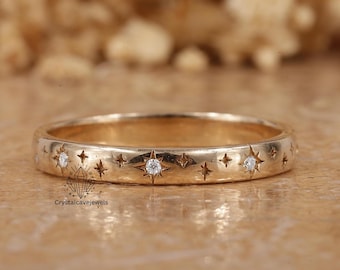 Op de afbeelding: Een goudkleurige ring met een band versierd met sterren en kleine diamanten. De ring heeft een gepolijste afwerking. De achtergrond is wazig. De ring is een sieraad.