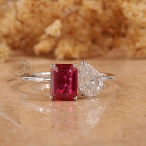 May include: A silver ring featuring a red emerald-cut gemstone and a pear-shaped diamond.
