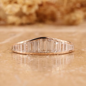 May include: A rose gold band ring with a row of baguette-cut diamonds set in a curved, slightly pointed design.