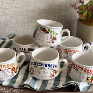 May include: A set of six white ceramic soup mugs, each featuring a unique recipe printed on the front. The mugs are labelled Mushroom, Oxtail Soup, Onion Soup, Chicken Soup, Scotch Broth, and Tomato Soup, with colourful illustrations of ingredients.