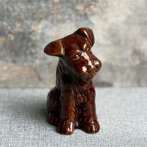 May include: A glossy, brown ceramic dog ornament in a seated pose. The dog has floppy ears and a detailed, textured coat. The figurine is a decorative item, likely for display.