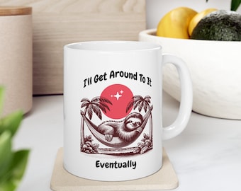 May include: White ceramic mug featuring a brown sloth illustration in a hammock with palm trees and a red sun. The text "I'll Get Around To It Eventually" is printed on the mug.