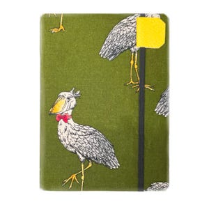 May include: A green notebook with a whimsical bird pattern. The birds are depicted in white and gray with yellow beaks and legs, and a red bow tie. A black elastic band and a yellow tab are visible on the right side.
