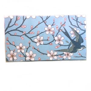 May include: Rectangular card with a light blue background featuring a floral design of white cherry blossoms and a dark blue bird in flight. The branches are brown, and the blossoms have pink centers.