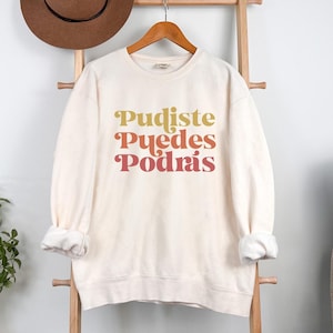 Può includere: Felpa color avorio con il testo "Pudiste Puedes Podrás" in un gradiente di giallo, arancione e rosso.