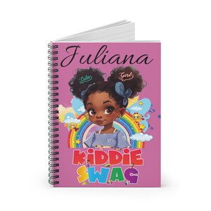 May include: Spiral-bound notebook with a pink cover featuring a cartoon illustration of a young girl with dark curly hair. The notebook has the name "Juliana" and the words "Cute" and "Girl" on the cover, along with the text "Kiddie Swag".