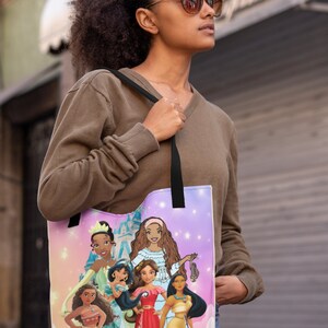 Pu&ograve; includere: Una borsa tote con sfondo rosa e viola che presenta un gruppo di principesse Disney. Le principesse indossano tutte abiti diversi e hanno acconciature diverse. La borsa ha spalline nere.