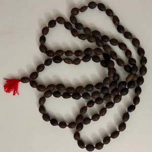 May include: A brown wooden mala bead necklace with a red tassel. The beads are oval shaped and strung together with a red thread.