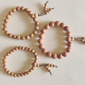 May include: Three wooden bead bracelets in varying shades of brown. Each bracelet is strung on a black cord and features a tassel detail. The beads are smooth and round, creating a natural and earthy aesthetic. Perfect for everyday wear.