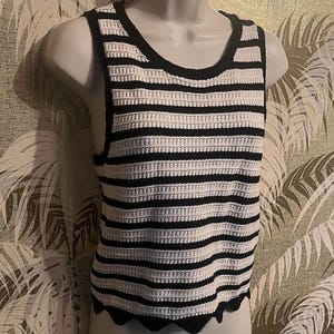May include: A sleeveless, horizontally striped top in black and white. The top has a rounded neckline and a scalloped hem. The fabric appears to be a knitted or crocheted material. The top is displayed on a white mannequin.