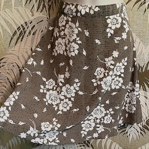 May include: A-line skirt with a brown background and a white floral pattern. The skirt has a high waist and falls to the mid-thigh. The floral design is a repeating pattern of large and small flowers.