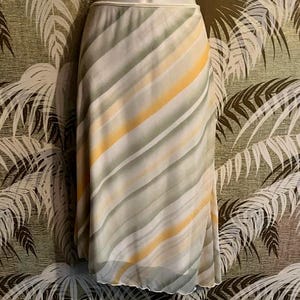 May include: A flowing, knee-length skirt with a diagonal striped pattern in shades of gray, yellow, and white. The skirt has a soft, lightweight appearance and a subtle sheen. The waistband is a solid, light color.