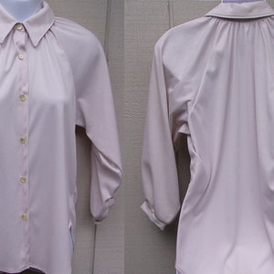 May include: A light pink button-down blouse with long sleeves and a collared neckline. The blouse is displayed on a mannequin, showcasing the front and back views. The fabric appears to be a smooth, lightweight material.