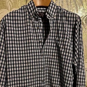 May include: A long-sleeved button-down shirt featuring a navy blue and white gingham check pattern. The shirt includes a pointed collar with buttons, a front button placket, and a single chest pocket on the left side with a small embroidered logo.