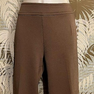 May include: Brown textured pants with a high waist. The pants have a subtle pattern and a tailored fit. The fabric appears to be a medium-weight material, suitable for various occasions. The pants are shown against a patterned background.