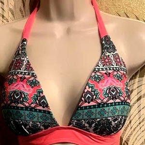 May include: A halter-style bikini top featuring a vibrant multi-colored pattern with shades of coral pink, teal, black, and white. The garment has solid coral pink straps and a matching solid coral pink band along the bottom edge.