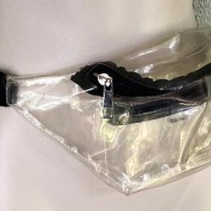 May include: A clear fanny pack with a black zipper and black adjustable strap. The transparent bag is made of a flexible material and has a zippered compartment. The fanny pack is designed to be worn around the waist.