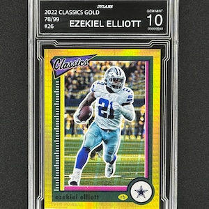May include: A gold-colored 2022 Classics Gold trading card of Ezekiel Elliott, graded Gem Mint 10. The card features Elliott in a Dallas Cowboys uniform, running with the ball. The card is encased in a clear protective holder.
