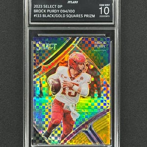 May include: A graded trading card featuring Brock Purdy, a football player for the Iowa State Cyclones. The card is a 2023 Select Draft Pick, numbered 094/100, and is a Black/Gold Squares Prizm. The card is graded Gem Mint 10.